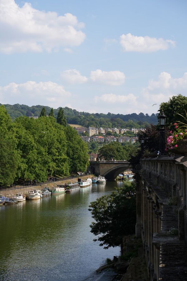 A river in Bath with moored boats and a bridge in the distance